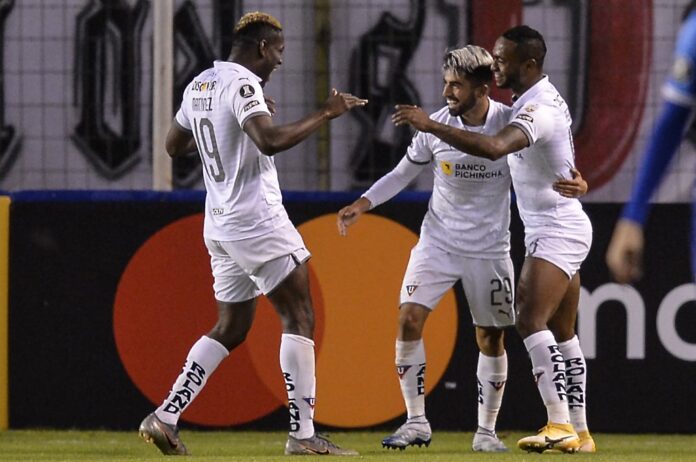 Três jogadores de futebol comemorando um gol em campo.