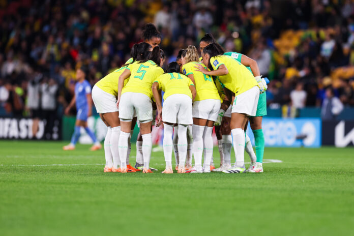 A seleção brasileira de futebol feminino se aglomera em campo.