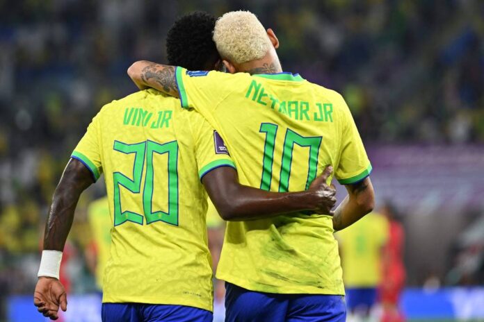 Dois jogadores de futebol, entre eles Vinicius Júnior, abraçados em campo.