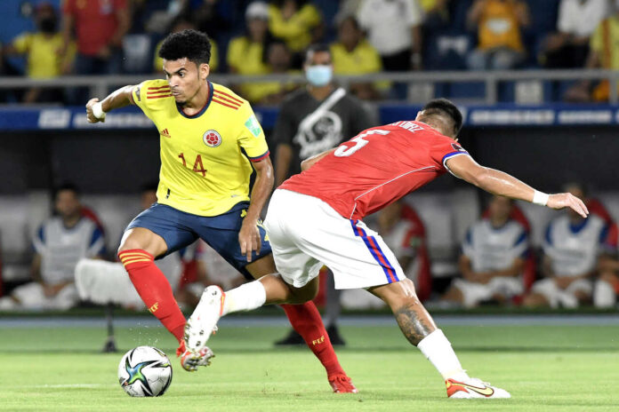 Dois jogadores de futebol do Chile e da Colômbia em ação durante uma partida, um controlando a bola enquanto o outro tenta defender.