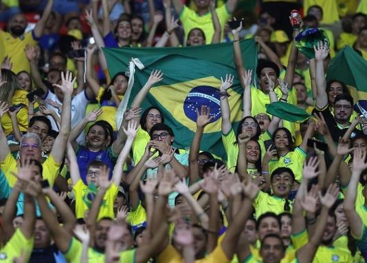 Torcedores entusiasmados em trajes amarelos e verdes torcendo em evento esportivo das Eliminatórias Sul-Americanas.