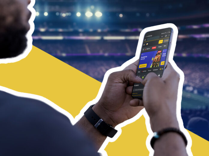 Homem usando um smartphone com um aplicativo de apostas esportivas em um evento no estádio.